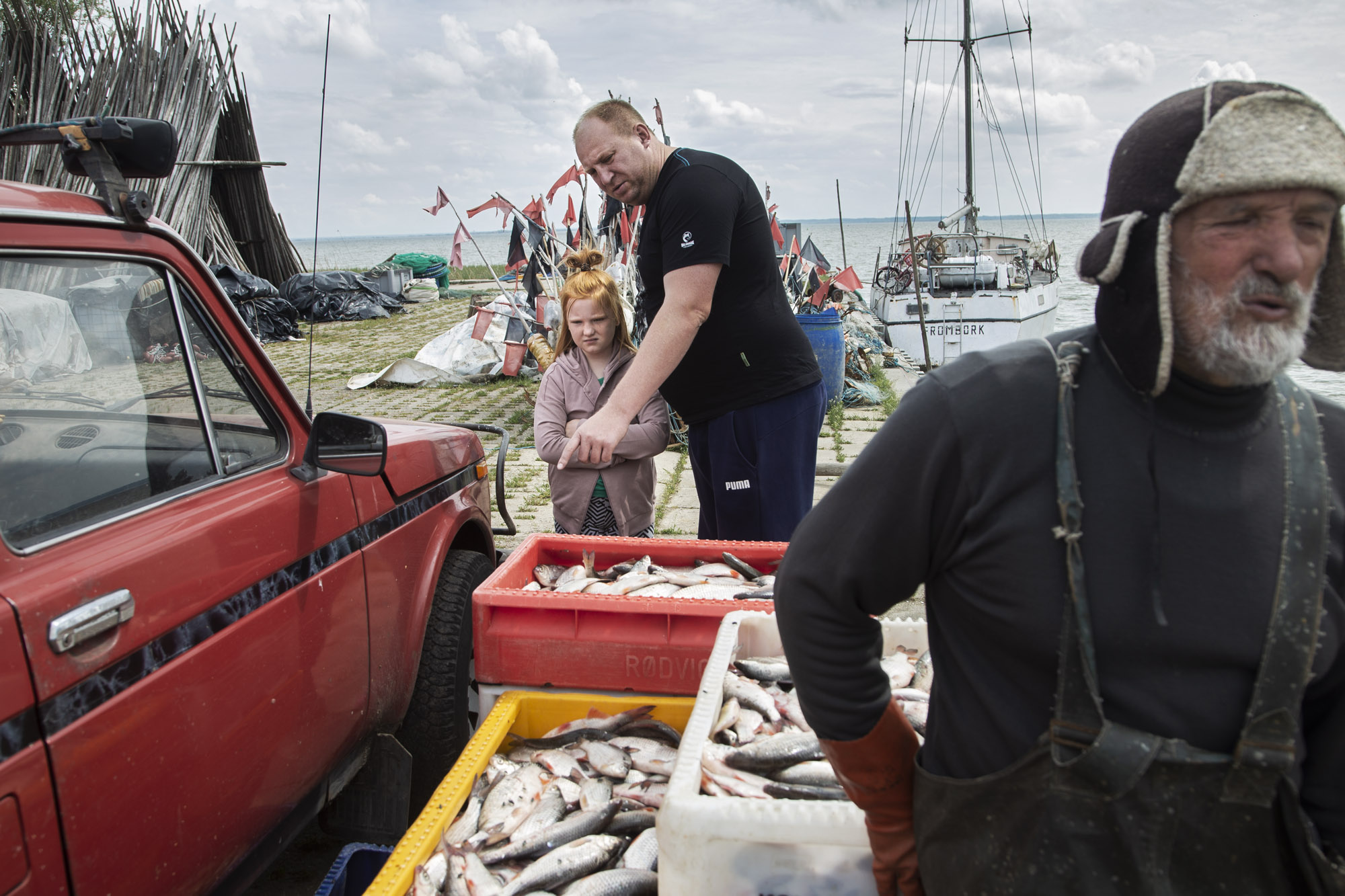 2021.05.16. Port w Piaskach na Mierzei Wislanej. Bracia Waldemar (z prawej) i Krzysztof Gotkowscy po polowie wyladowuja ryby z lodzi. W porcie czeka juz na nich niewielka grupka turystow, ktorzy kupuja ryby "z burty", czyli bezposrednio do rybakow.  